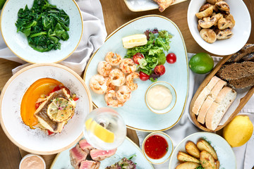 Many different delicious dishes dishes on the table. Various snacks and antipasti on the table. Plates seafood BBQ with garnish. Variety of dishes on the table. Restaurant menu.