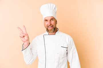 Chef man isolated on beige background joyful and carefree showing a peace symbol with fingers.