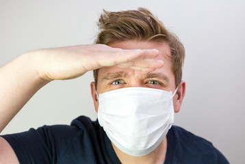 Man with mask to protect him from virus. The concept of the epidemic of the coronavirus. Tired Doctor with medical white mask. I don't see, where are you. Man looking far away