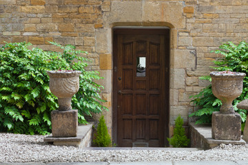Fototapeta na wymiar Dark brown old doors in an old traditional English stone house with evergreen plants and ornamental pots in the front .