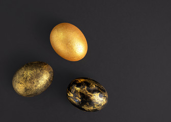 Three Easter eggs in gold and black colors are on a dark background.