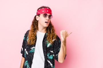 Young hippie caucasian man isolated points with thumb finger away, laughing and carefree.