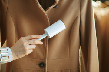 Closeup on woman cleaning coat with lint roller
