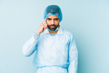 Young surgeon latin man isolated Young dpointing temple with finger, thinking, focused on a task.