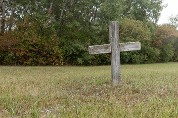As simple wooden cross marking a lonely grave in a grassy field.  The single grave creates a sad...
