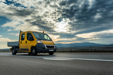 Fototapeta na wymiar Yellow Mini Truck - Utility transportation van or mini truck driving through highway with dramatic sunset sky in the background. Transportation vehicle