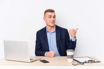 Young business man with a laptop points with thumb finger away, laughing and carefree.