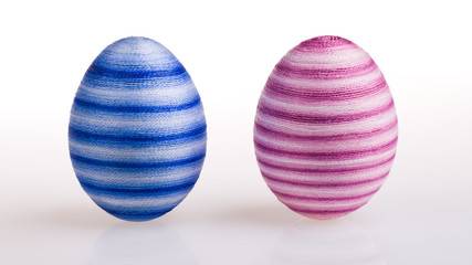 Two standing Easter eggs striped in male blue and female pink color on white background. Creative decoration. Colored streaked chicken egg shells closeup wrapped by glued thin cotton yarn. Front view.