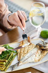 Lunch in a restaurant, a woman eats roasted dorado fish with grilled asparagus. Dish decorated with a slice of lemon. Restaurant menu