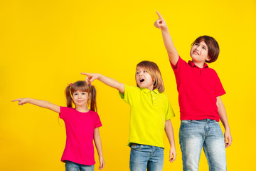 Pointing. Happy children playing and having fun together on yellow studio background. Caucasian kids in bright clothes looks playful, laughting, smiling. Concept of education, childhood, emotions.