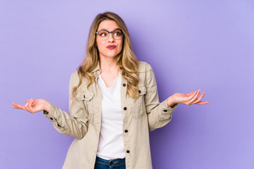 Fototapeta na wymiar Young caucasian woman isolated on purple background doubting and shrugging shoulders in questioning gesture.
