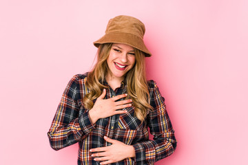 Young caucasian woman wearing a hat isolated laughs happily and has fun keeping hands on stomach.