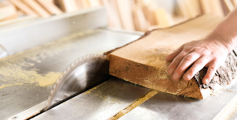 Worker hands details of wood cutter machine with a circular saw and wooden board. Circular cutting saw in action.