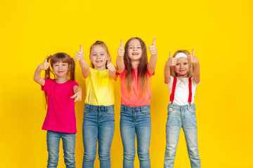 Thumbs up. Happy children playing and having fun together on yellow studio background. Caucasian kids in bright clothes looks playful, laughting, smiling. Concept of education, childhood, emotions.