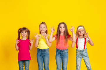 Nice gesture. Happy children playing and having fun together on yellow studio background. Caucasian kids in bright clothes looks playful, laughting, smiling. Concept of education, childhood, emotions.