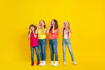 Fototapeta premium Calling. Happy children playing and having fun together on yellow studio background. Caucasian kids in bright clothes looks playful, laughting, smiling. Concept of education, childhood, emotions.
