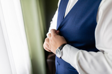 Man in a white shirt and a blue vest is buttoning a vest. A stylishly dressed businessman adjusts the buttons on his vest.