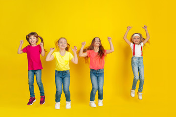 Fototapeta premium Jumping. Happy children playing and having fun together on yellow studio background. Caucasian kids in bright clothes looks playful, laughting, smiling. Concept of education, childhood, emotions.