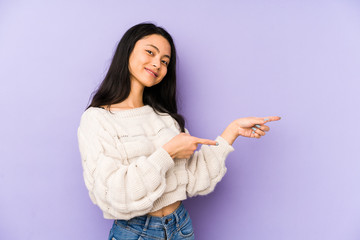 Young chinese  woman isolated on a purple background excited pointing with forefingers away.