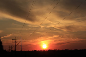 sunset over a field with clouds and Power Lines with the Sun in Kansas.
