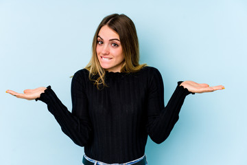 Young caucasian woman isolated on blue background confused and doubtful shrugging shoulders to hold...