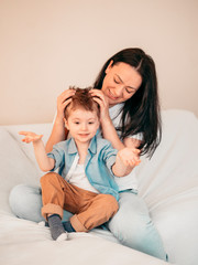 Mother and her little 4 years son sitting on sofa, Mother straightens baby hair. Mother's day concept