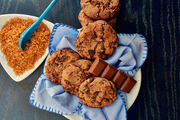 plate of cocoa cookies, brown cane sugar and chocolate, with blue tones on napkin, wooden table, tablecloth and spoon
