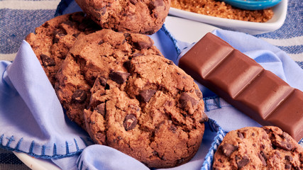 plate of cocoa cookies, brown cane sugar and chocolate, with blue tones on napkin, wooden table, tablecloth and spoon