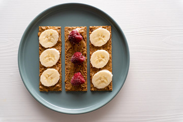 Closeup. Raspberry, peanut butter and banana on small bread slices on round plate on white background, toast for morning breakfast or snack for brunch, minimal concept, healthy eating, toned