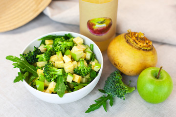 Fresh spring green vegetable salad on a table with apples, turnips, arugula, broccoli on a light background. Farm organic product, home-made