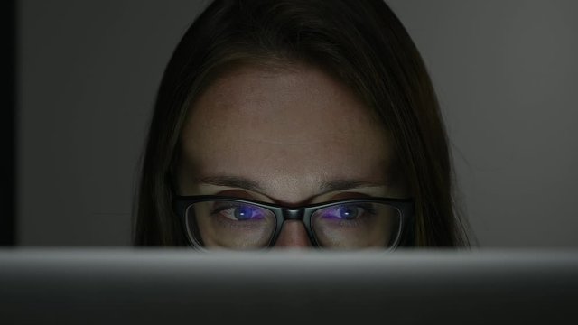 woman in glasses sitting at a laptop at night in an apartment