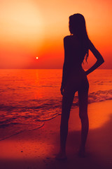 Fototapeta premium Black slhouette of slim girl on the sea beach. People meets the dawn. Summer vacation.