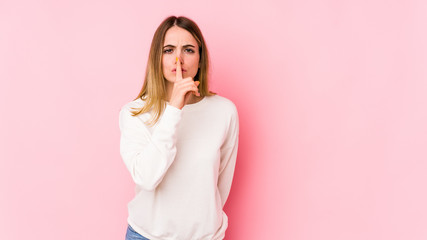 Young caucasian woman isolated on pink background keeping a secret or asking for silence.