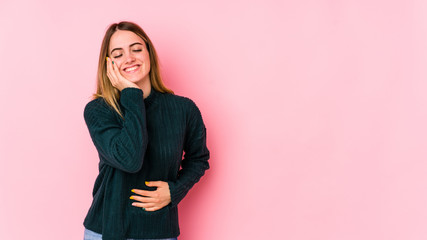 Young caucasian woman isolated on pink background laughs happily and has fun keeping hands on stomach.