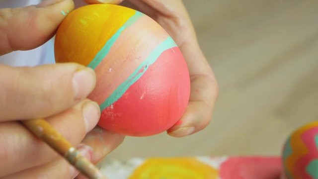 Posting: a review of the eggs and the transition to the hands of the artist who paints the Easter egg. Girl draws a striped pattern on an egg. Easter decoration preparing happy easter