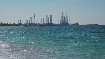 Construction of oil production towers in the Persian Gulf. Desert edifilled beach, waves. The concept of ocean pollution, global warming, carbon production.