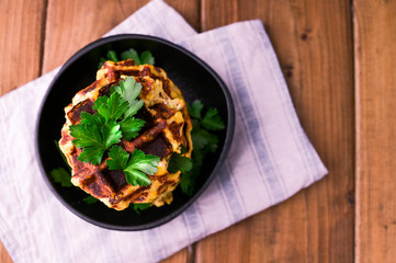 Lush belgian waffles with vegetables and herbs on a wooden table. The concept of a healthy diet and vegetarianism. Dark photo in rustic style. Free space for text.