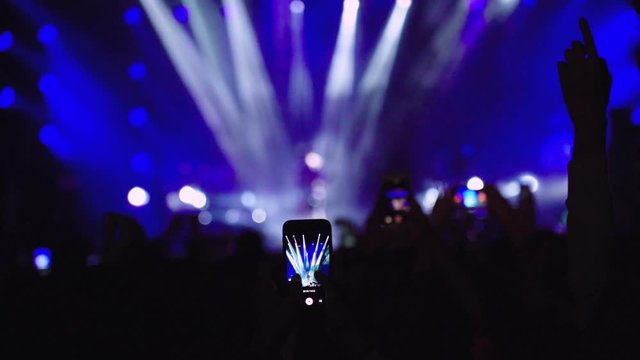 Music fan record video on phone in crowd on concert, closeup of audience people fans raise hands enjoy live music festival event shoot rock band stage on mobile device in purple lights, slow motion.