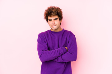 Young caucasian man against a pink background isolated frowning face in displeasure, keeps arms...