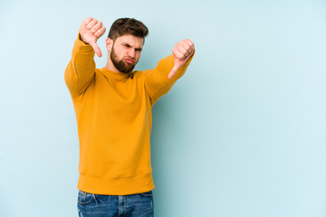 Young caucasian man isolated on blue background showing thumb down and expressing dislike.