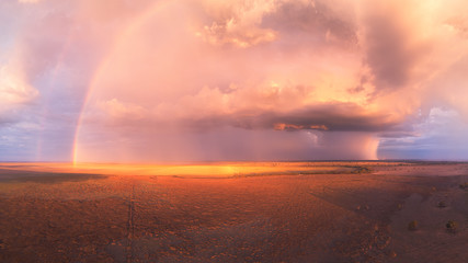 Stormy sunset with double rainbow, towering cumulus cloud and rain cells over a dry lake in...