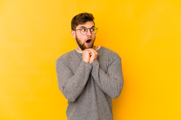 Young caucasian man isolated on yellow background praying for luck, amazed and opening mouth looking to front.