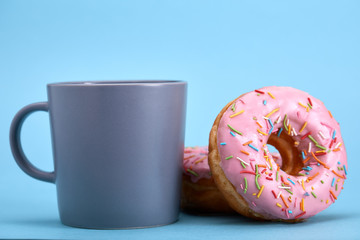 Sweet pink donuts with a blue mug on a blue background. Concept dessert, sweet life, we are what we eat. Blue background, copy space.