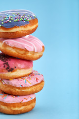 A stack of sweet donuts on a blue background. Concept desserts, different colored donuts laid out on top of each other by a tower. Copy space, blue background.