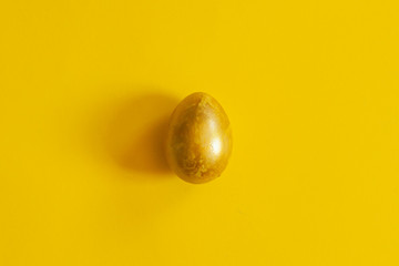 A single golden colored easter egg on the yellow background. View from above. Top view. Flat lay image of easter festive holiday background