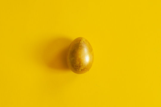 A single golden colored easter egg on the yellow background. View from above. Top view. Flat lay image of easter festive holiday background
