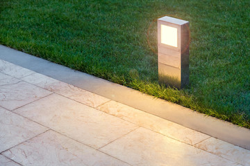 ground lamp lighting marble walkway in the evening park with a green lawn, closeup lantern...