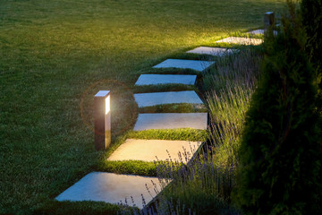 marble path of square tiles illuminated by a lamp glowing with a warm light in a night garden with...