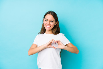 Young caucasian woman  isolated smiling and showing a heart shape with hands.