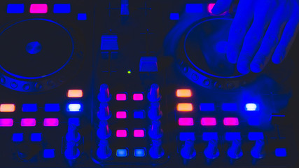 DJ plays music. sound mixer controller with knobs and sliders. hands on the mixing deck with turntables at dark with illuminated controls